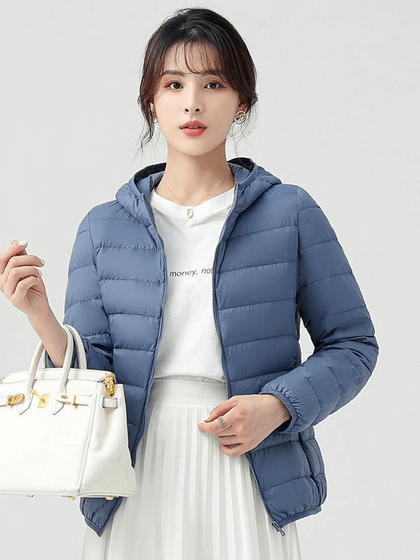 Woman wearing a stylish blue down jacket with hood, paired with a white skirt and carrying a white handbag, showcasing elegant outdoor fashion.
